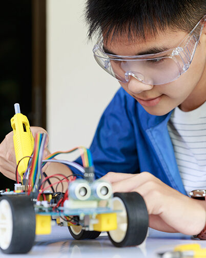 Young asian teen plugging energy and signal cable to sensor chip of toy car workshop.